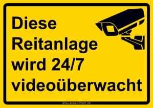 Ein gelbes Schild mit der Aufschrift Stallschild „Reitanlage wird 24/7 videoüberwacht“.